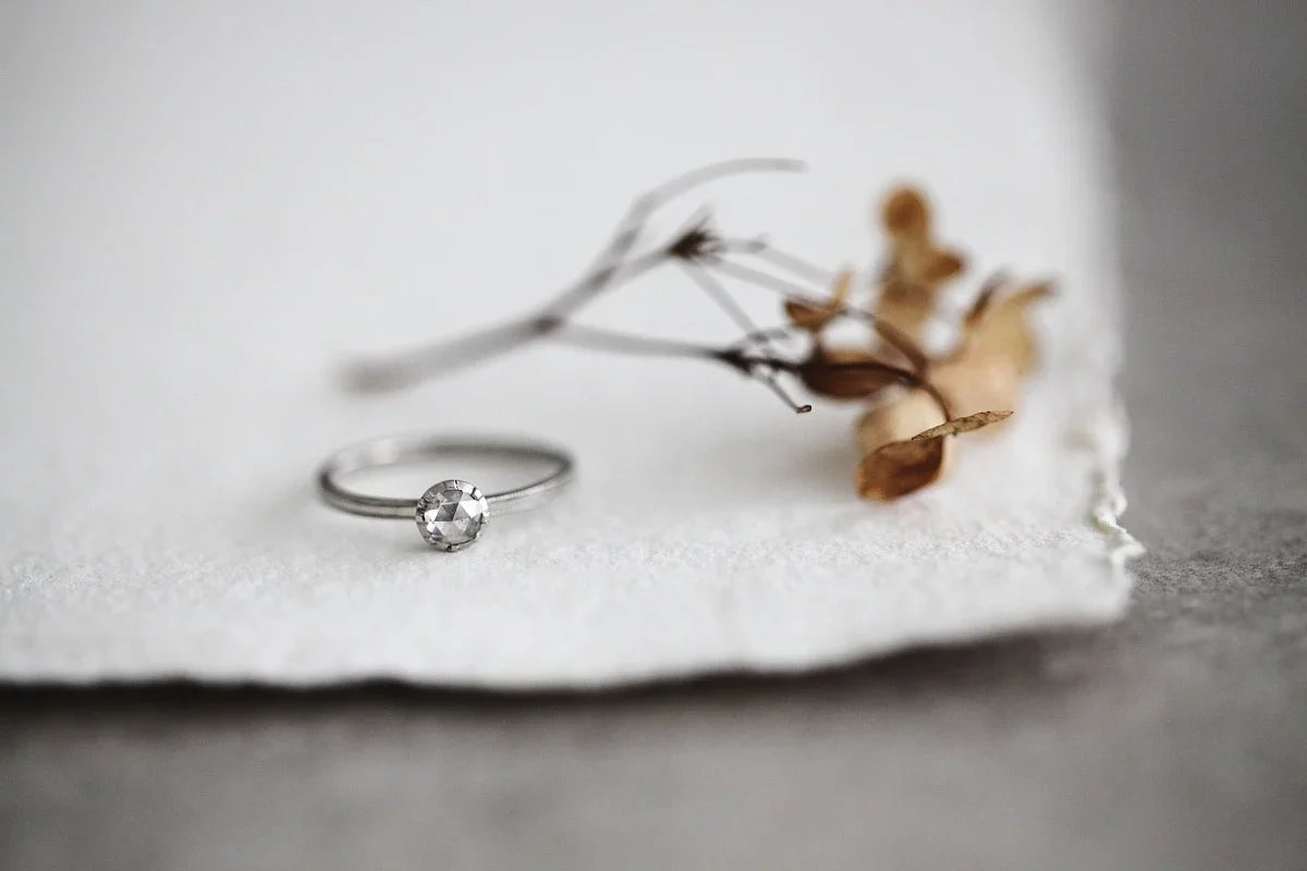 Silver ring with a diamond on a white cloth with dried flowers