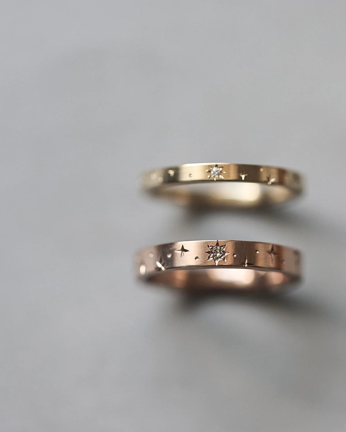 Two gold rings with engraved designs on a gray background