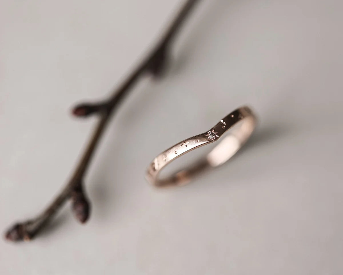 Rose gold ring on a light gray background with a blurred branch
