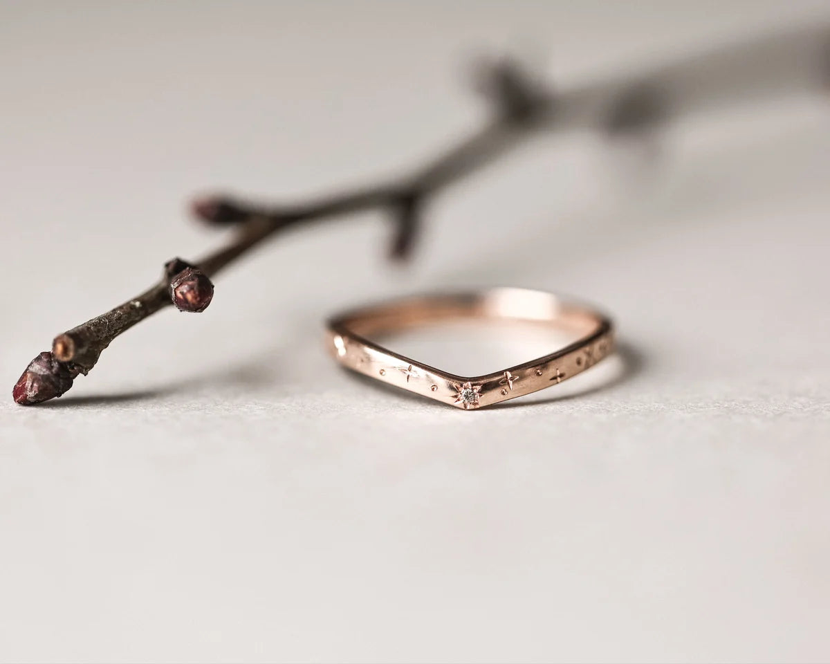 Rose gold ring on a light surface with a branch in the background