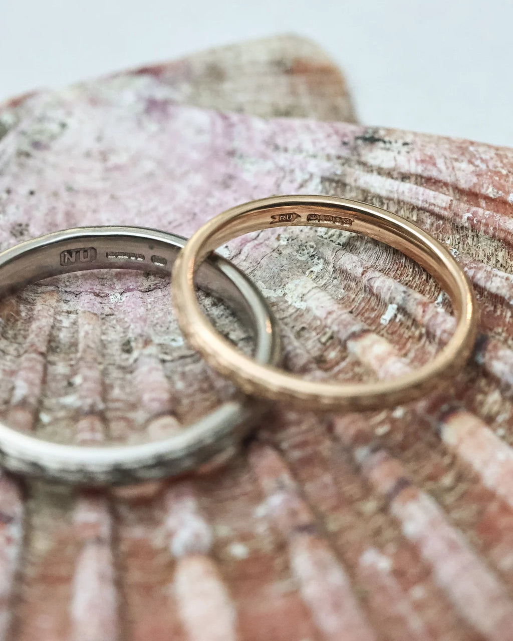 Two rings, one silver and one gold, on a textured surface.