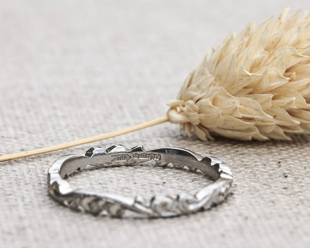 Silver ring with engraved design on a textured surface with dried flowers.