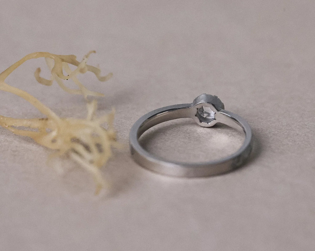 Silver ring with a small stone on a beige surface with a yellow flower.