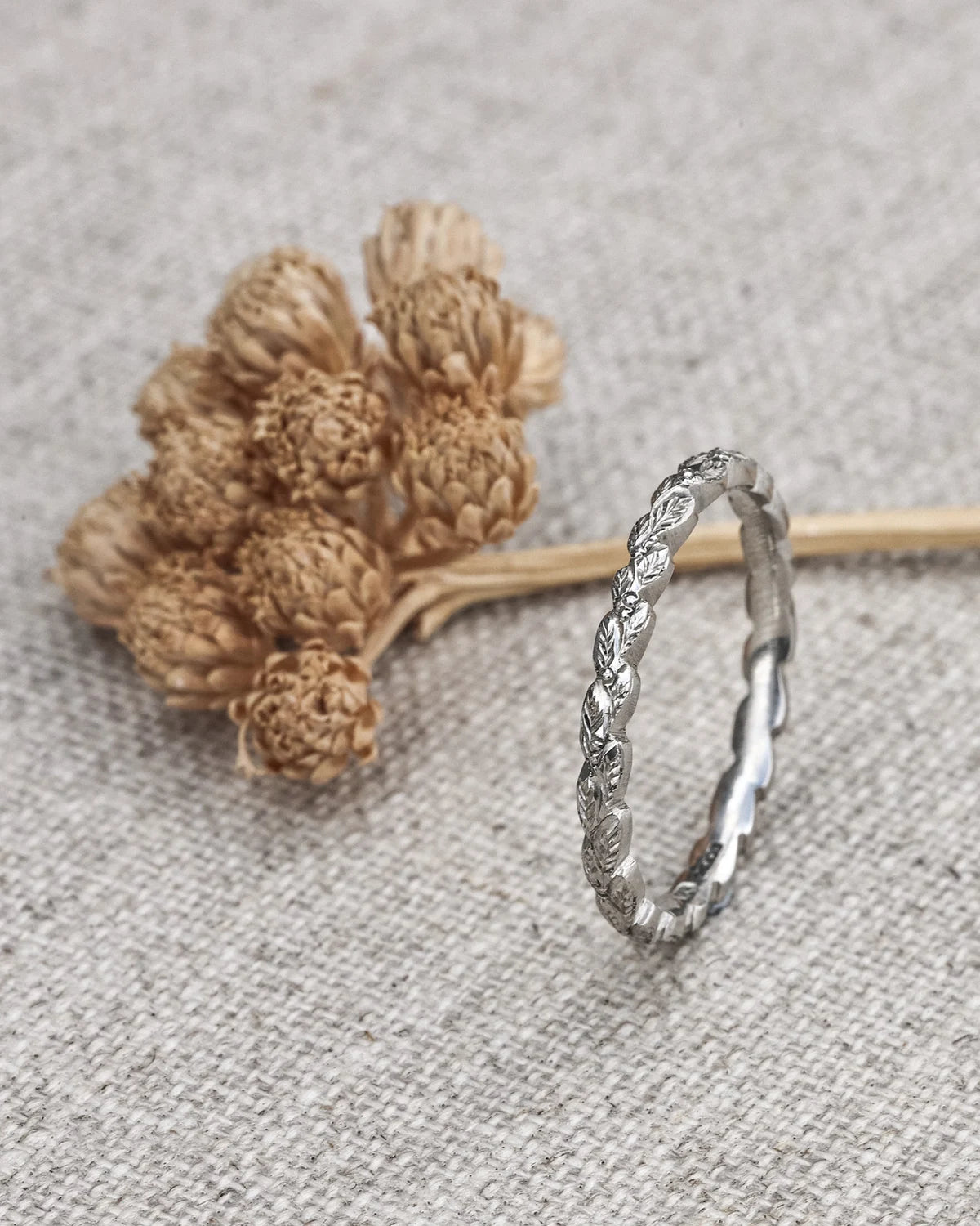 Silver ring with intricate design on a textured surface with dried flowers