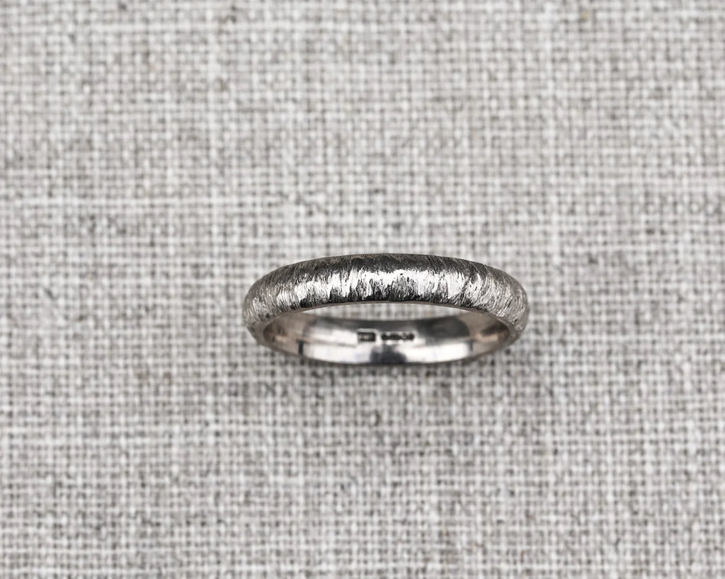 Silver ring with a textured surface on a gray fabric background