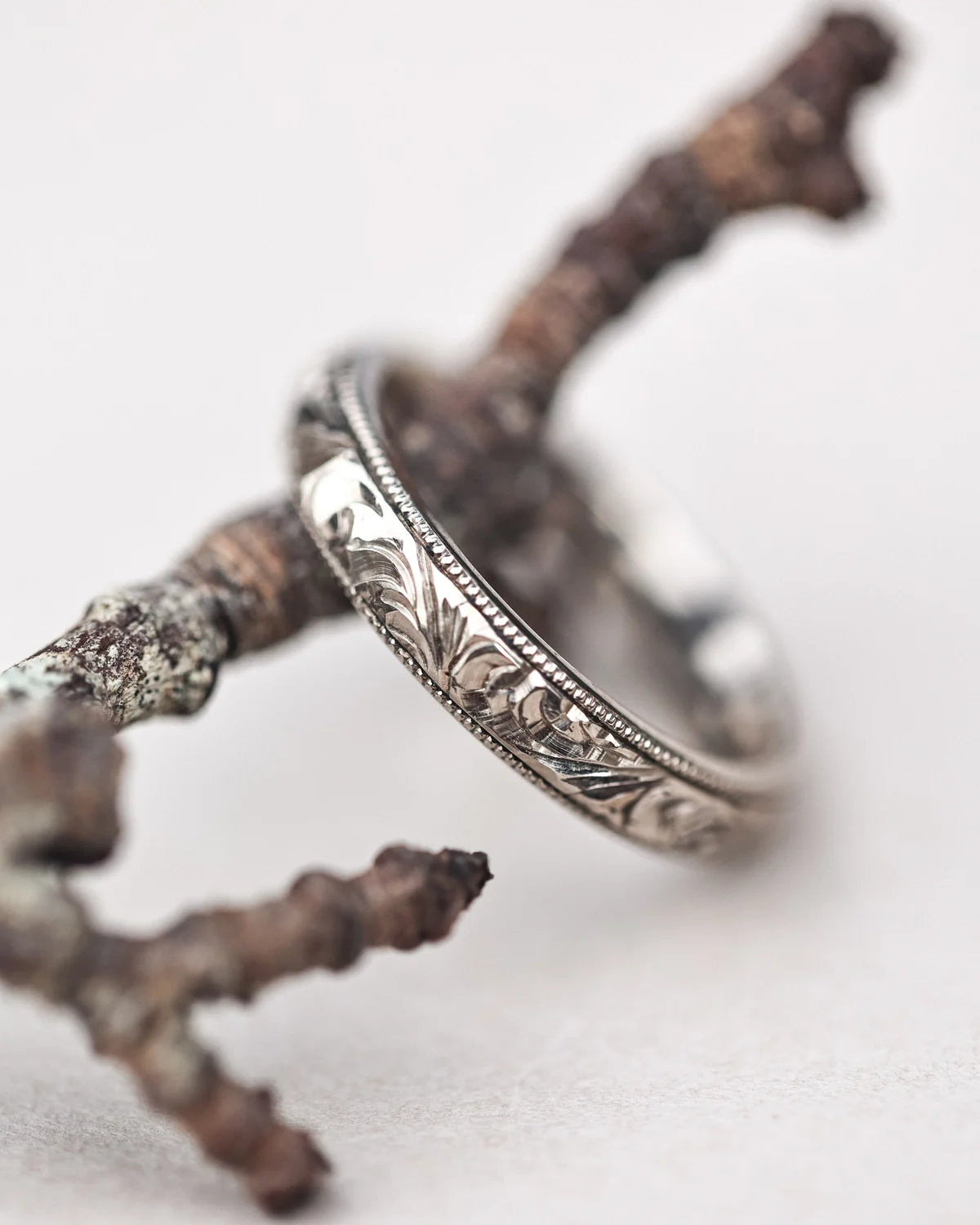 Floral engraved white gold wedding ring styled on natural branch