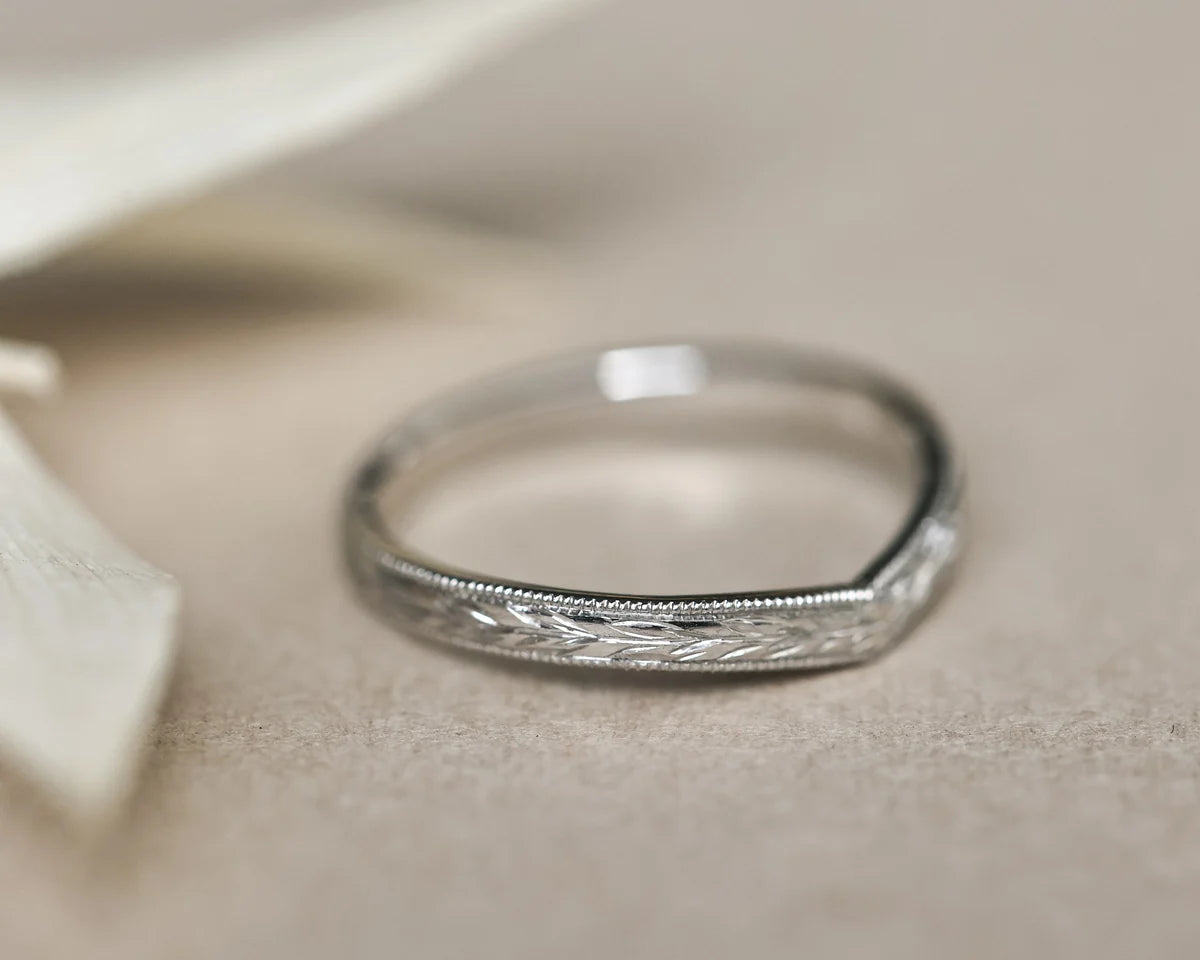 Close-up of platinum wishbone wedding band with hand engraved olive leaf motif
