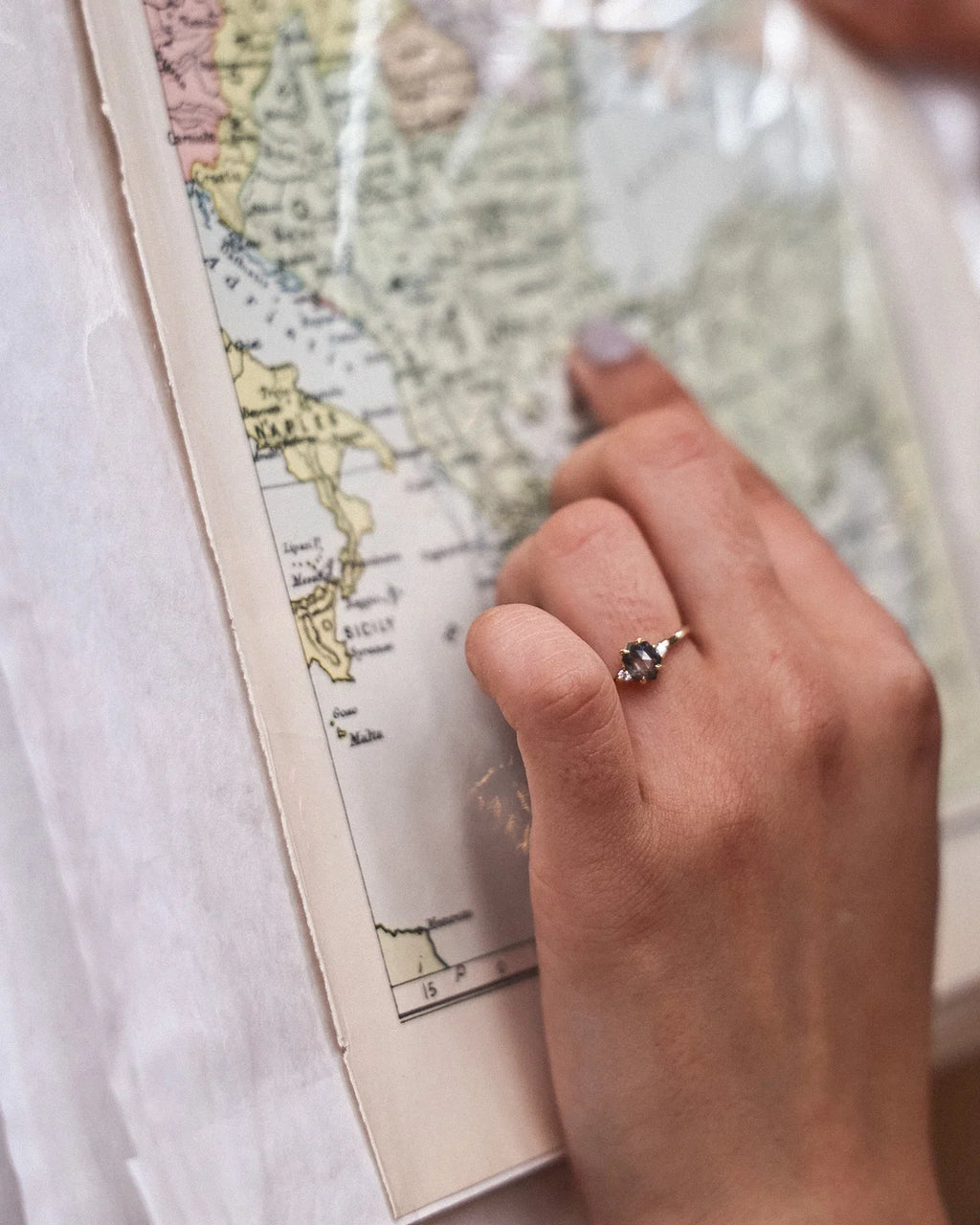 Grey diamond trilogy ring worn on hand over illustrated map