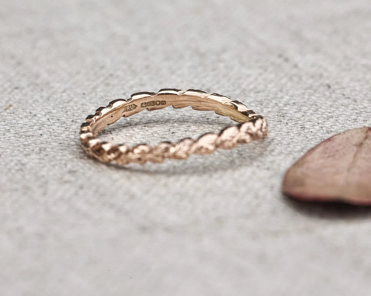 Rose gold ring on a textured gray surface with a leaf