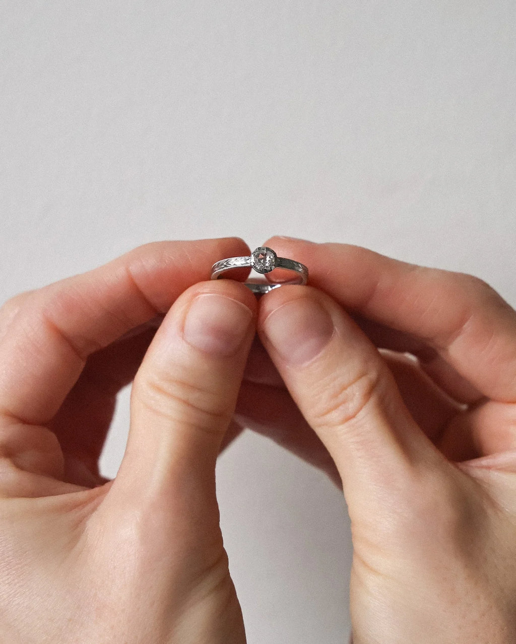 Close-up of a handmade platinum rose-cut diamond ring with engraved olive leaf band held by hand.