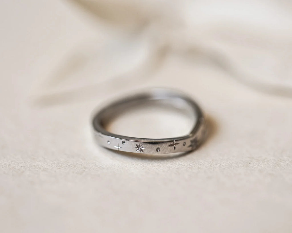 Silver ring with engraved patterns on a beige fabric background