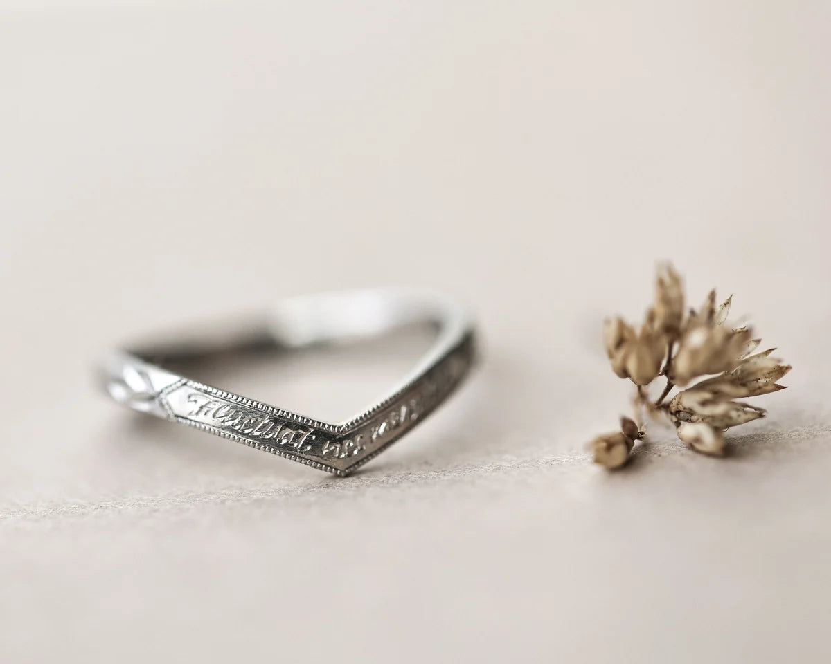Silver ring with engraved text next to a small dried flower on a light background