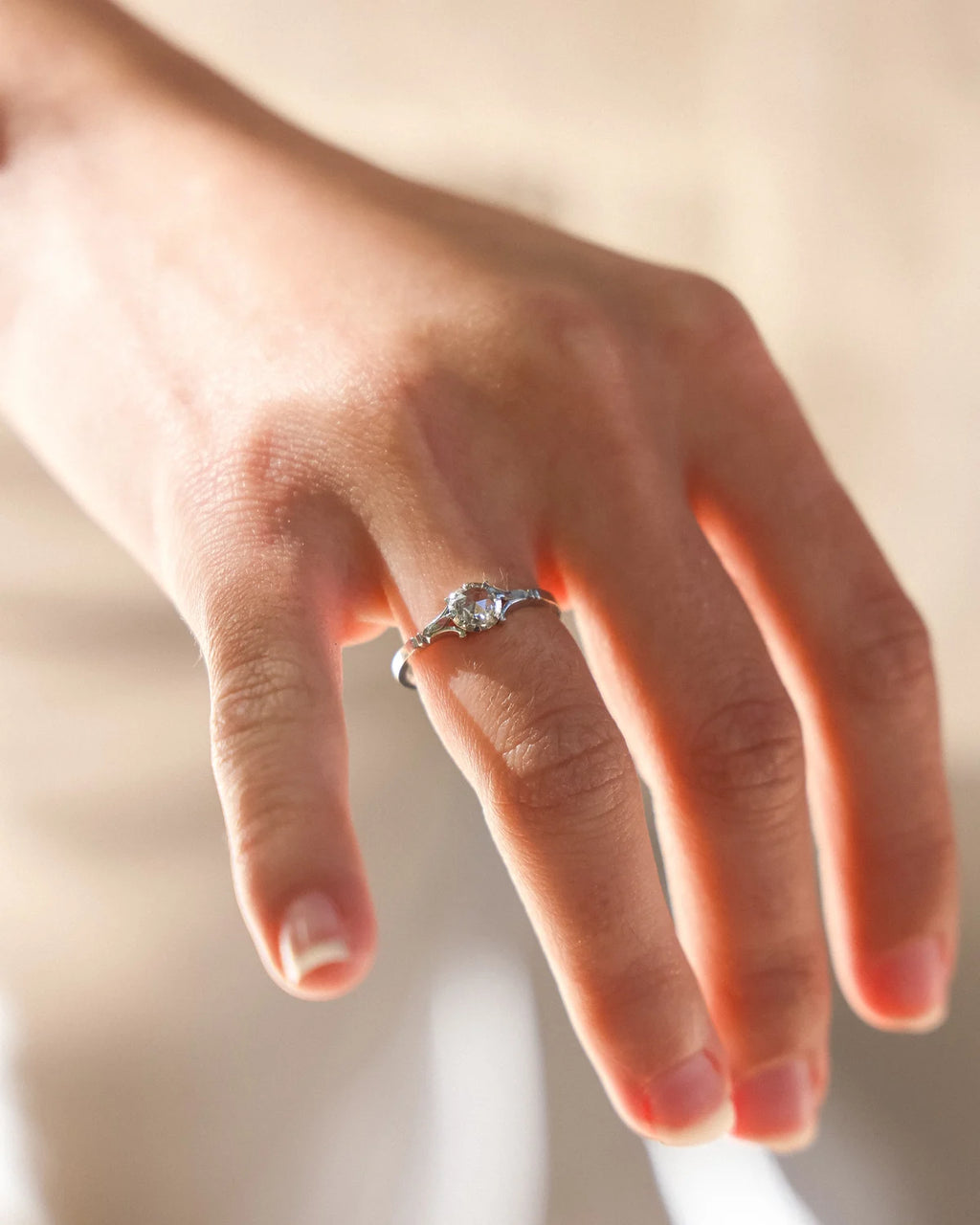 A silver ring with a central clear gemstone worn on a person's finger, shown in a warm, softly lit close-up shot.