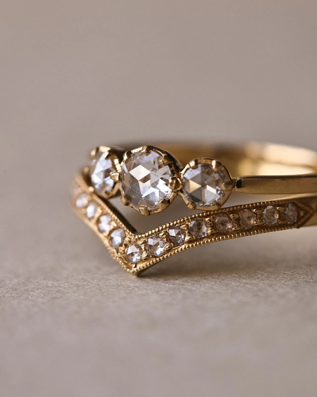 Close-up of rose-cut diamond trilogy ring stacked with pavé wishbone band