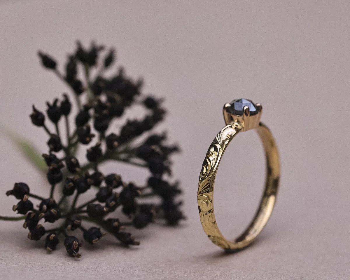 Portrait view of dark grey diamond ring with engraved gold band