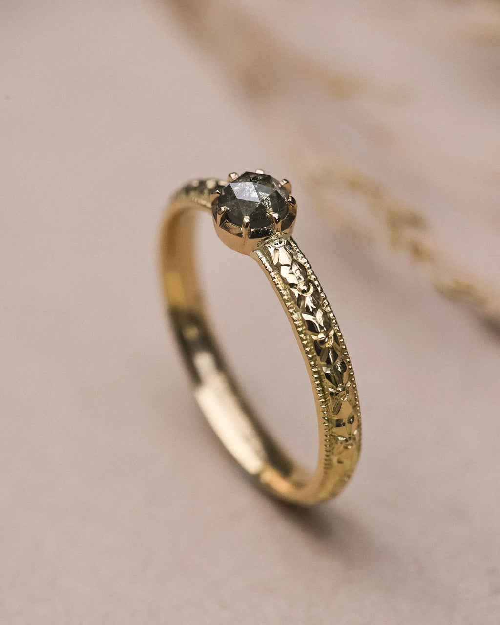 Angled view of handmade grey diamond ring with engraved botanical band