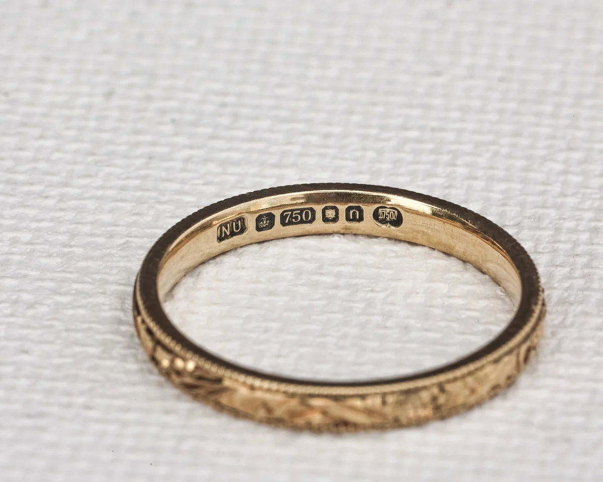 Gold ring with engraved details on a textured white background