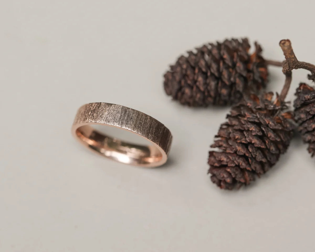 Angled view of 9ct rose gold horn texture wedding ring with pine cones