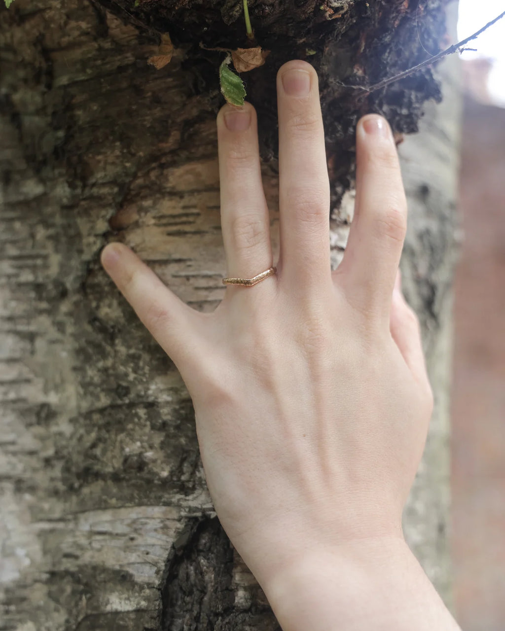 18ct rose gold wishbone ring worn on hand against tree bark