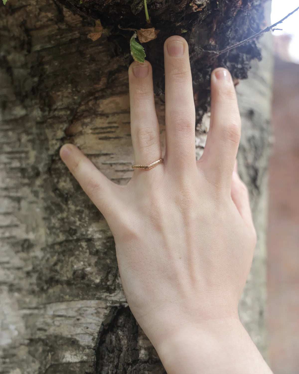 18ct rose gold wishbone ring worn on hand against tree bark