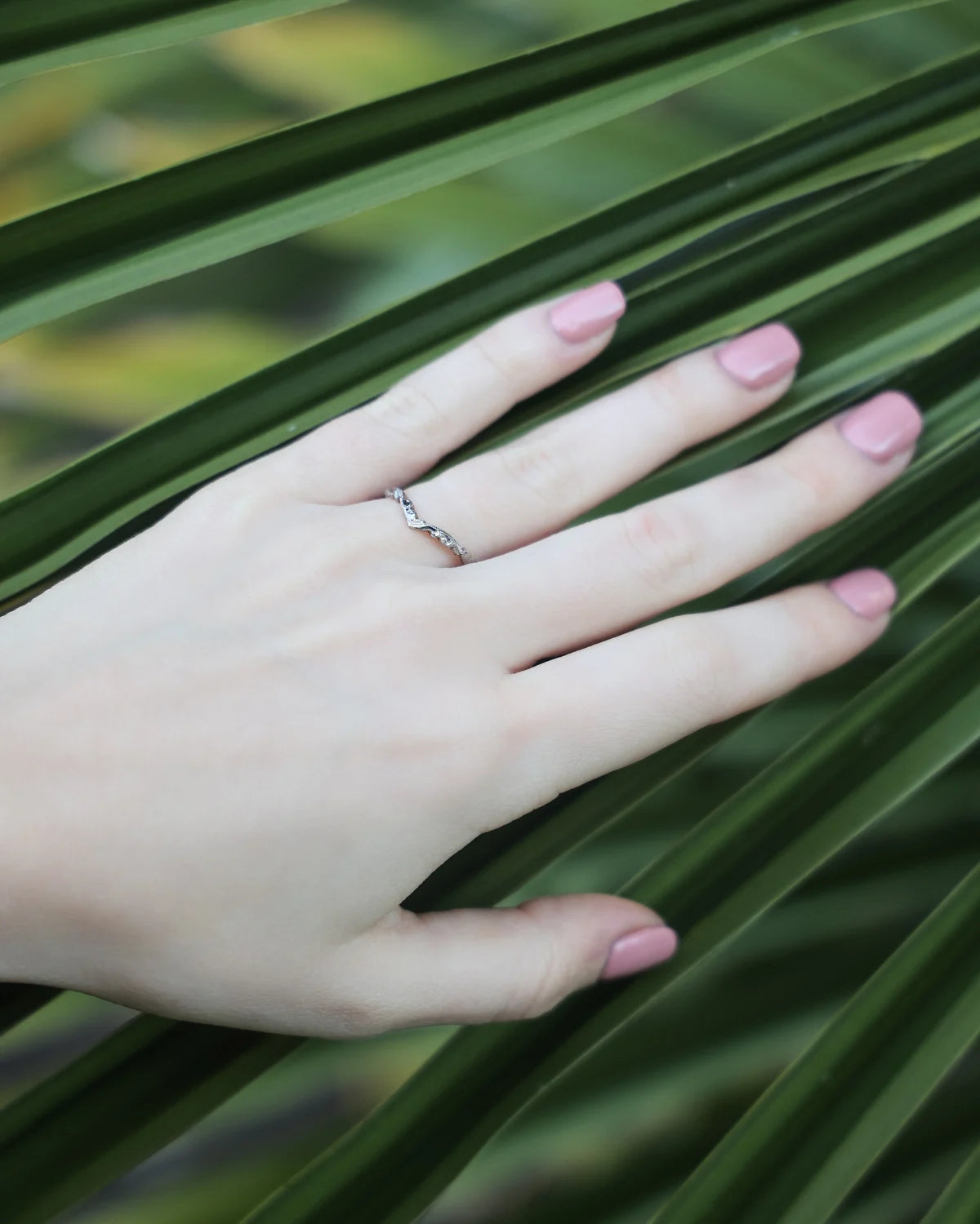 Engraved wishbone wedding ring worn on hand with pink nail polish