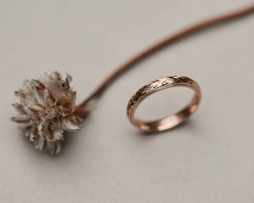 Angled view of olive leaf engraved rose gold wedding band