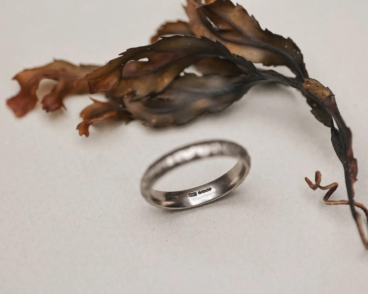 Silver ring on a textured surface with dried seaweed