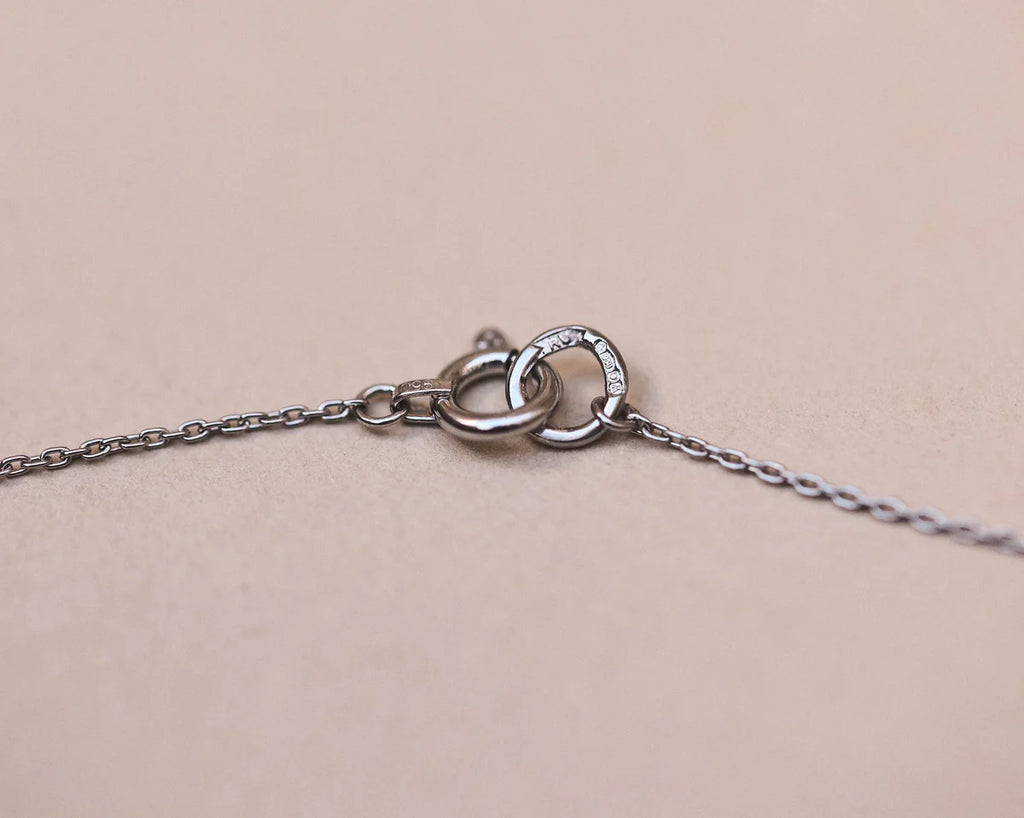 Close-up of a silver necklace with a clasp on a beige background