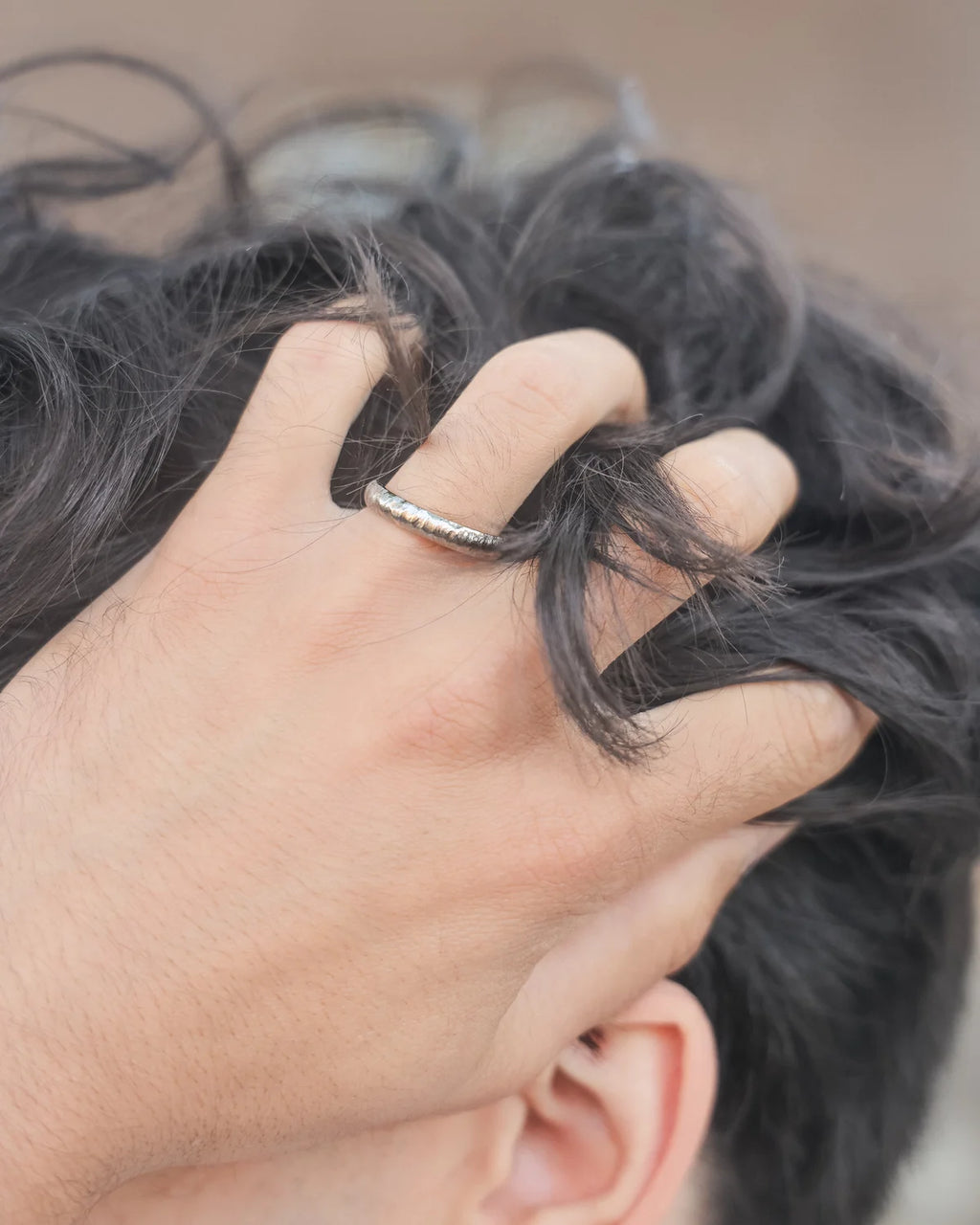 Person with a hand near their ear, wearing a silver ring.