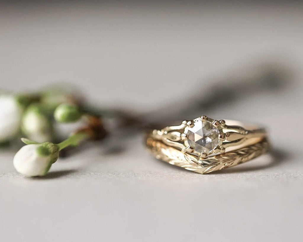 Gold ring with a diamond on a light surface with blurred flowers in the background