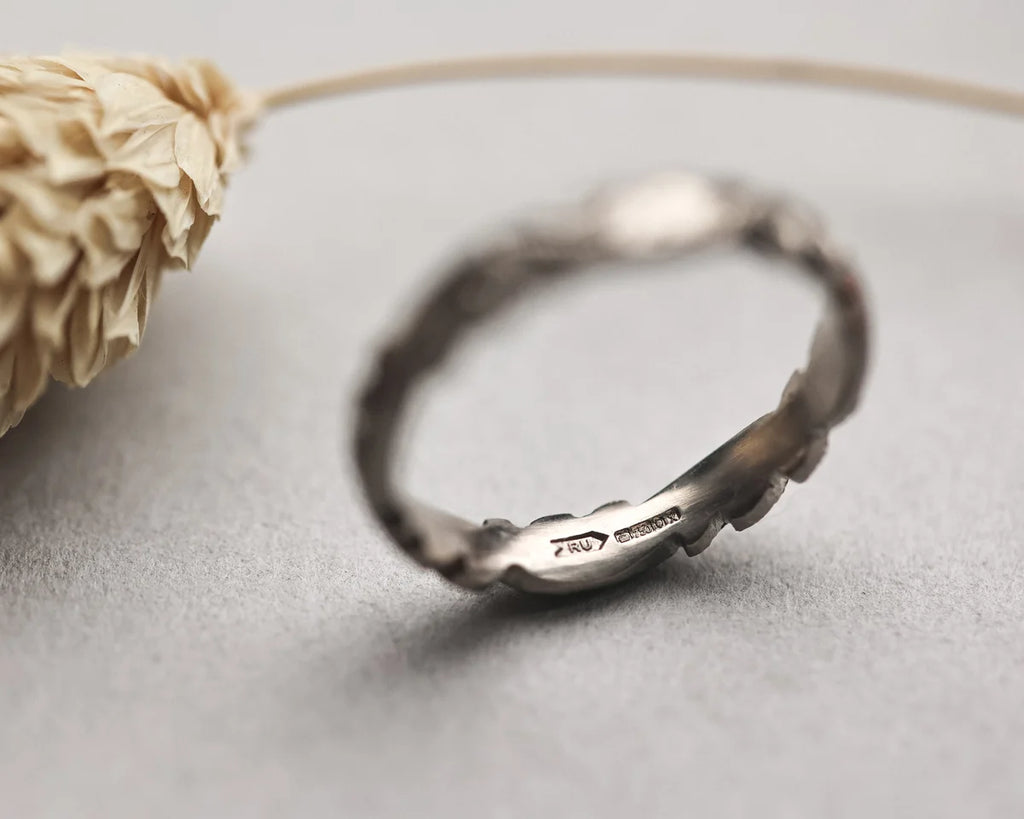 Silver ring on a light gray surface with a dried flower.