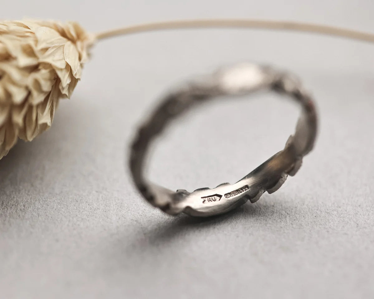Silver ring on a light gray surface with a dried flower.