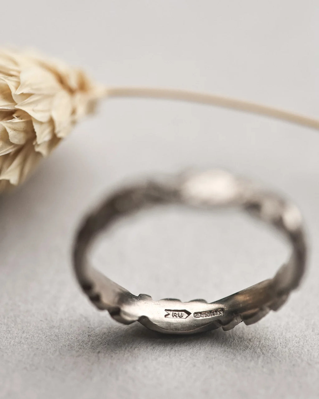 Silver ring with engraved design on a light gray surface with a dried flower.