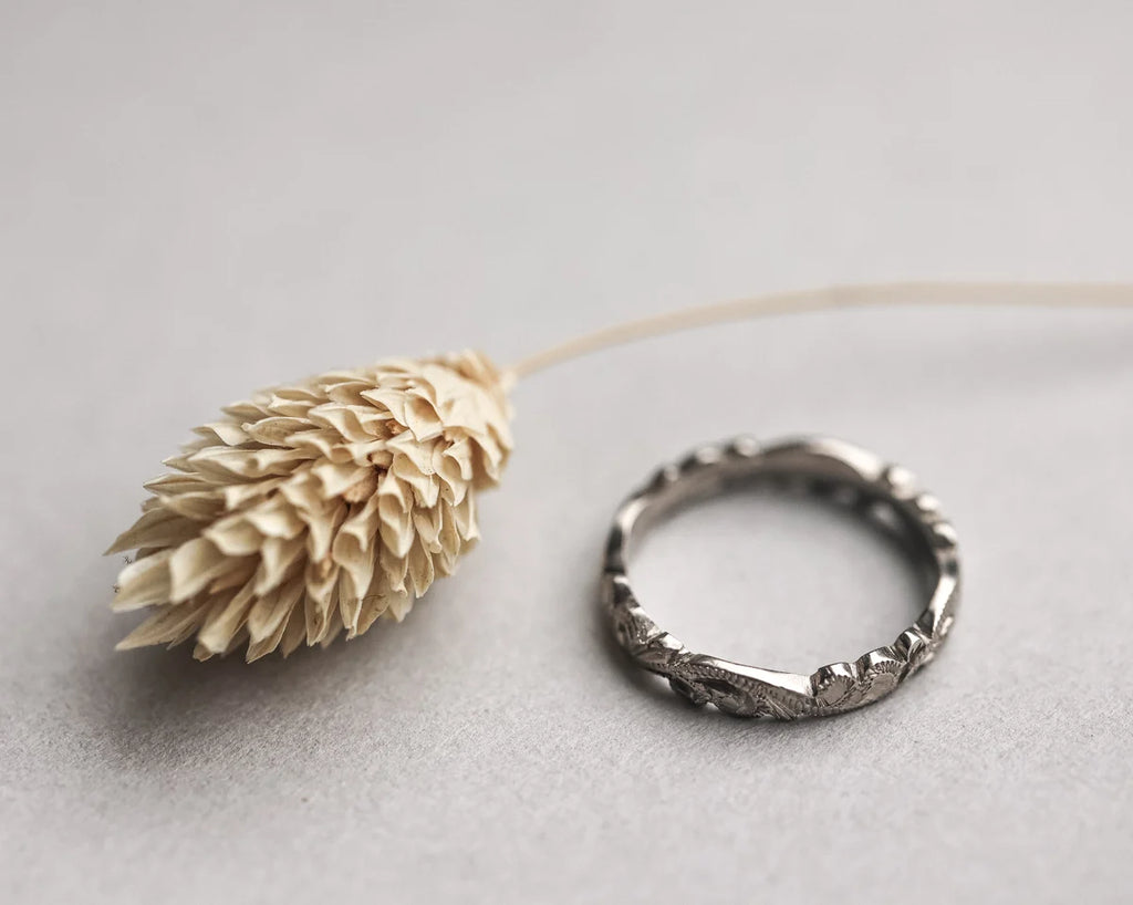 Silver ring on a light gray background with a dried plant