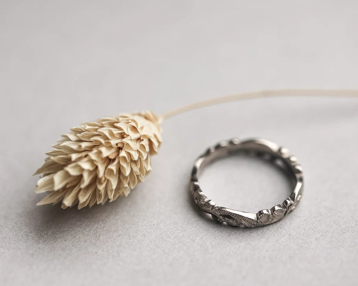 Silver ring on a light gray background with a dried plant