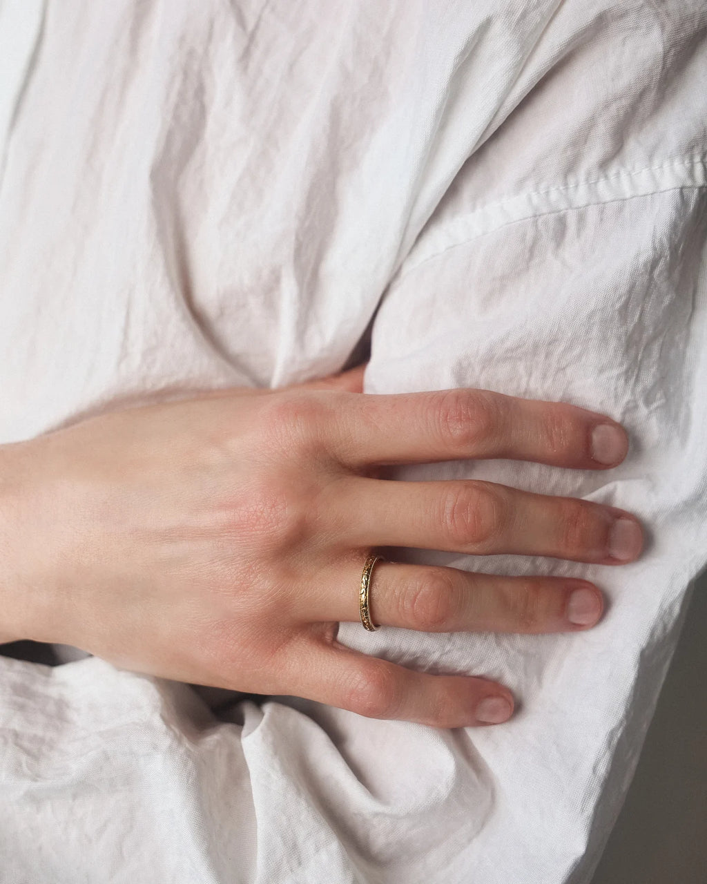 Hand wearing a gold ring on a white fabric background