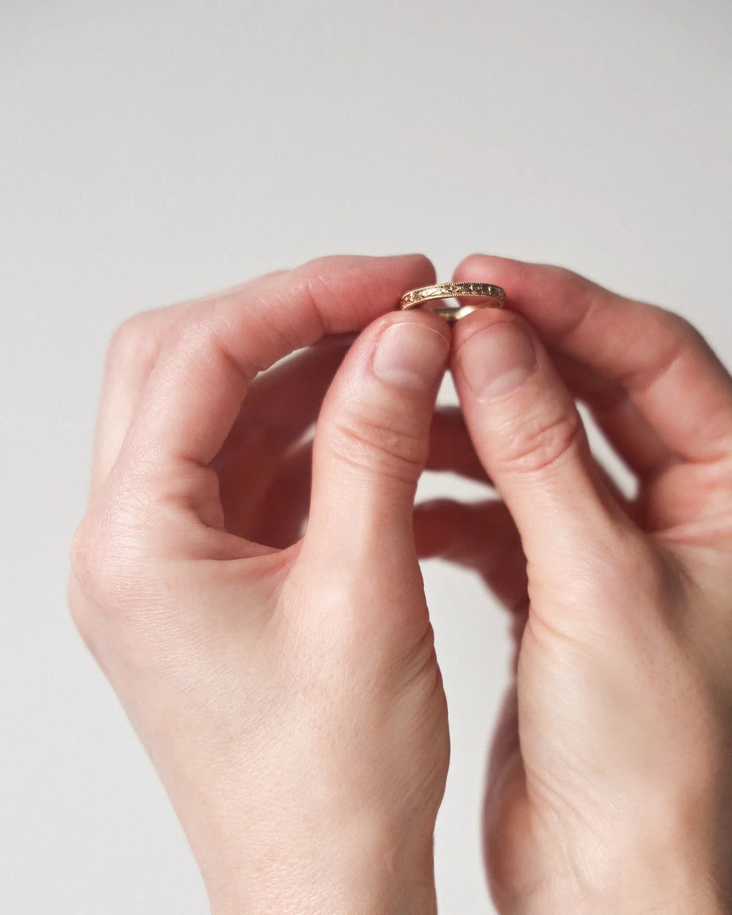 Close-up of hands holding a gold ring against a light background