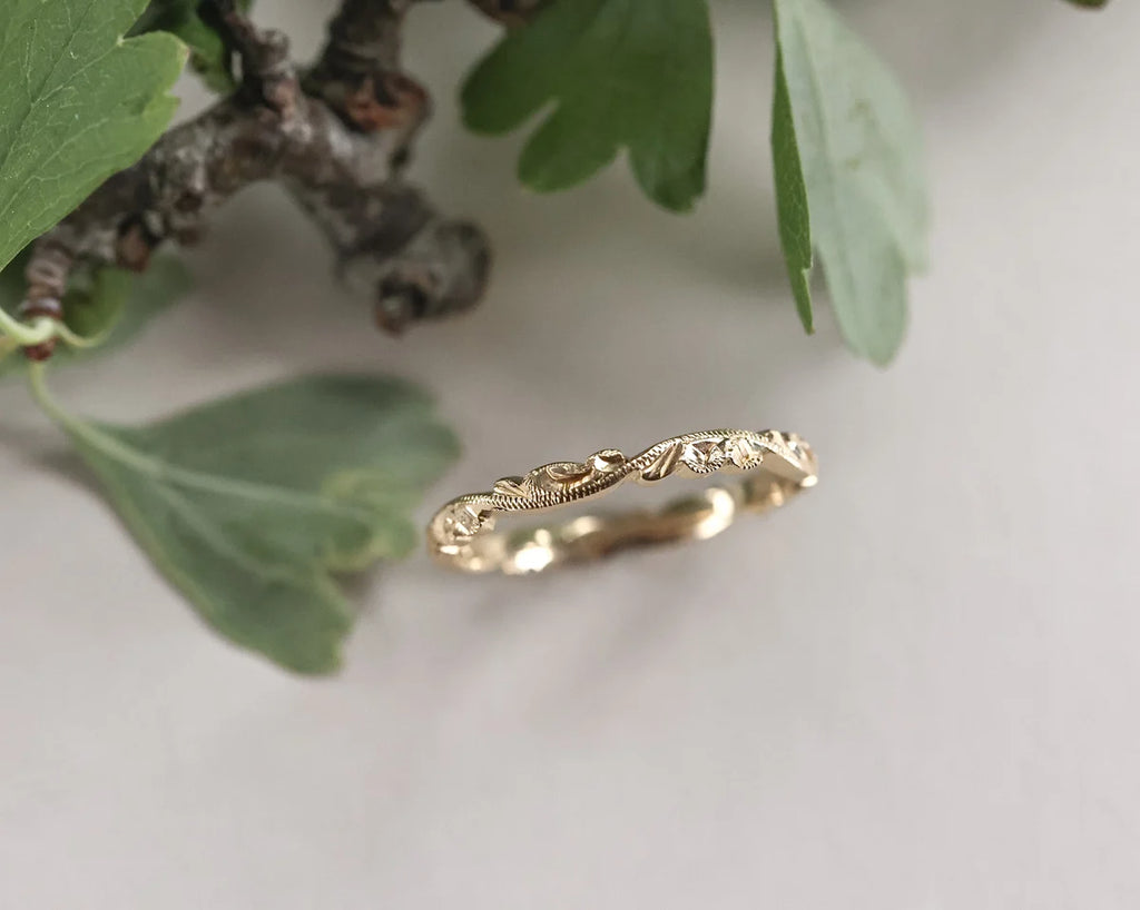 Gold ring with intricate design on a light background with green leaves