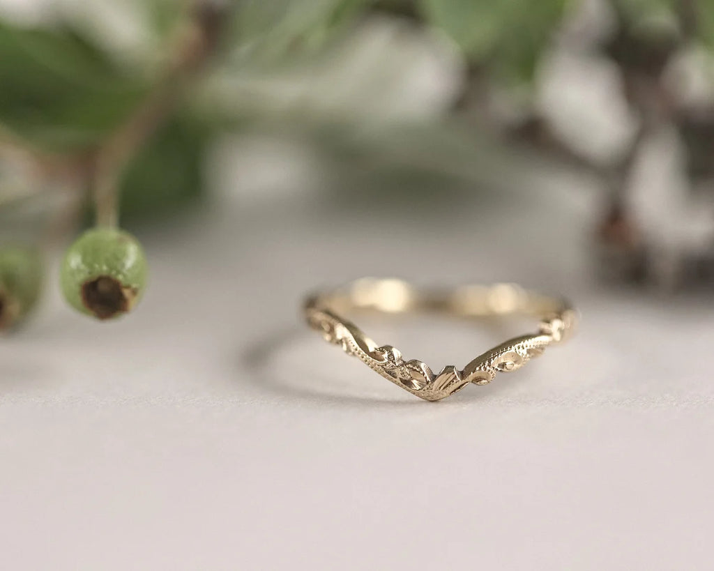 Gold ring with a mountain design on a white surface with greenery in the background