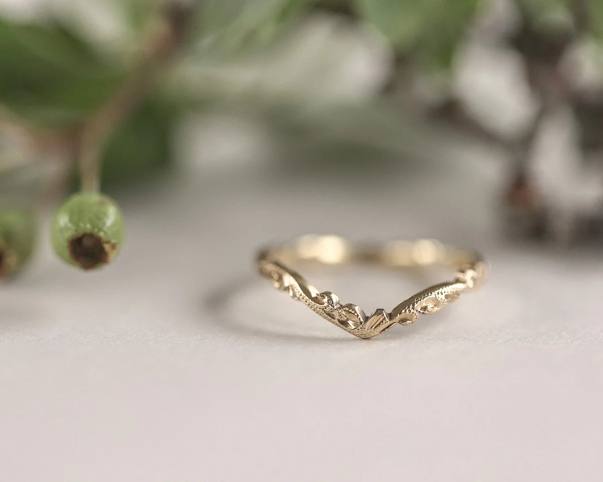 Gold ring with a mountain design on a white surface with greenery in the background