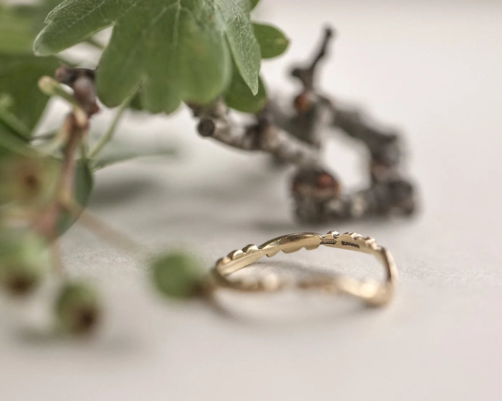 Gold ring with wavy design on a light background with greenery