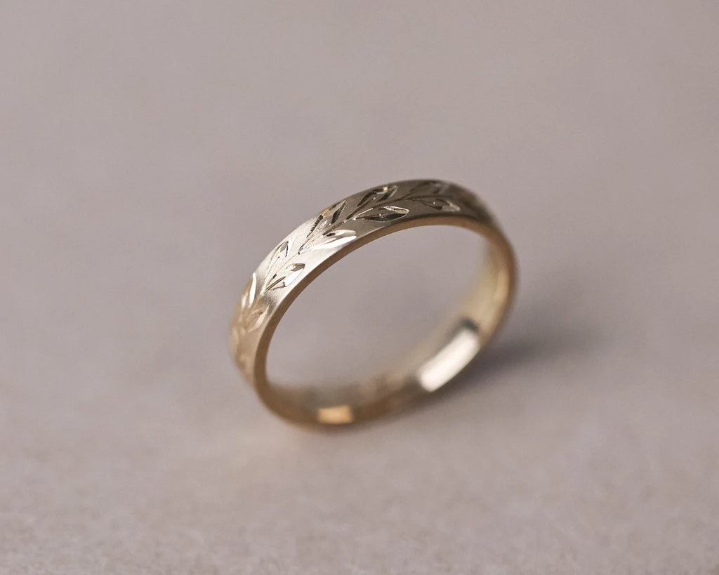 Angled view of 9ct yellow gold olive leaf engraved flat court wedding ring