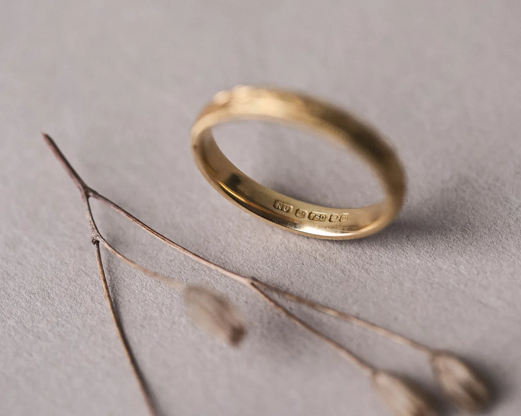 Gold ring on a gray surface with a branch and small flowers.
