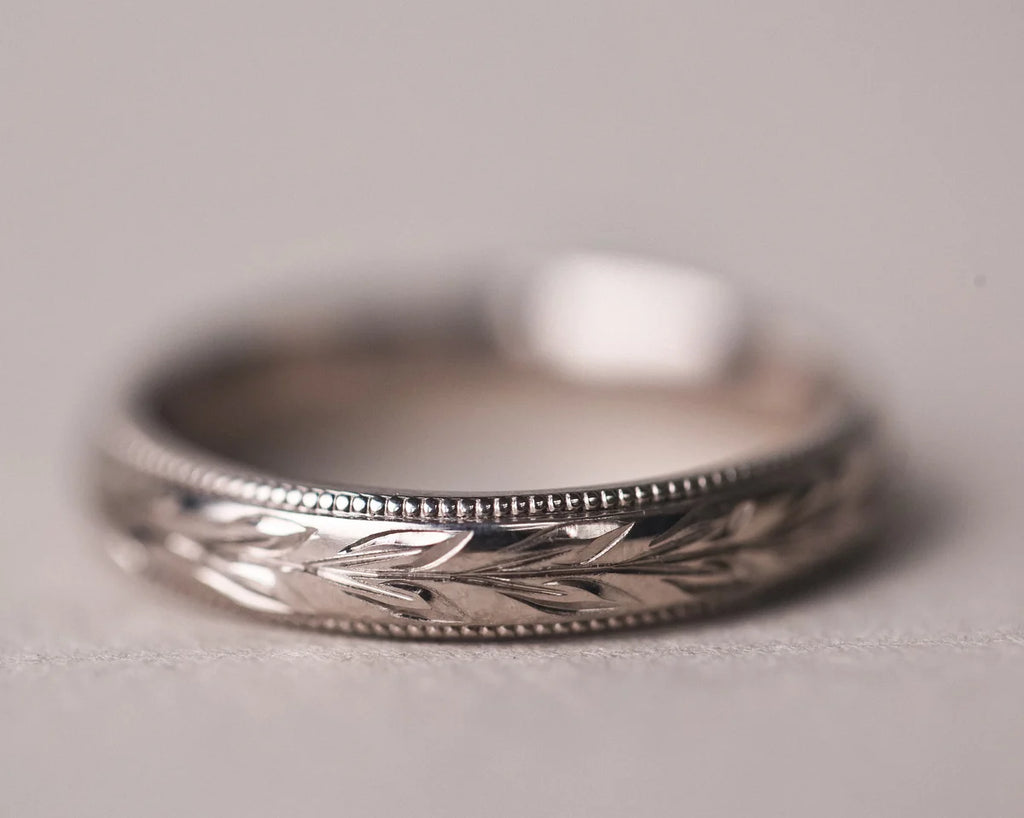 Close-up of 18ct white gold wedding ring with olive leaf engraving and milled edge
