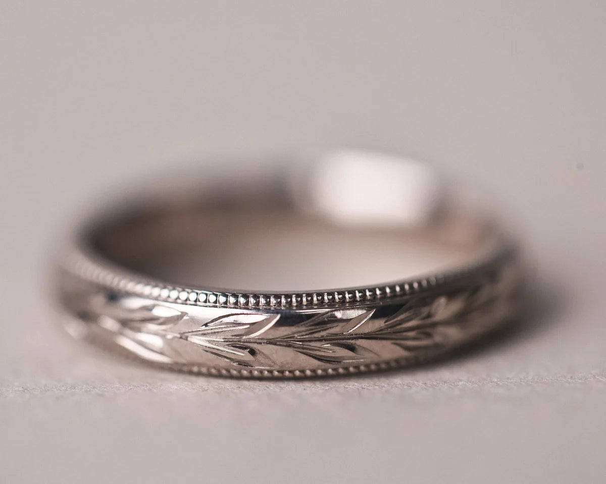 Close-up of 18ct white gold wedding ring with olive leaf engraving and milled edge