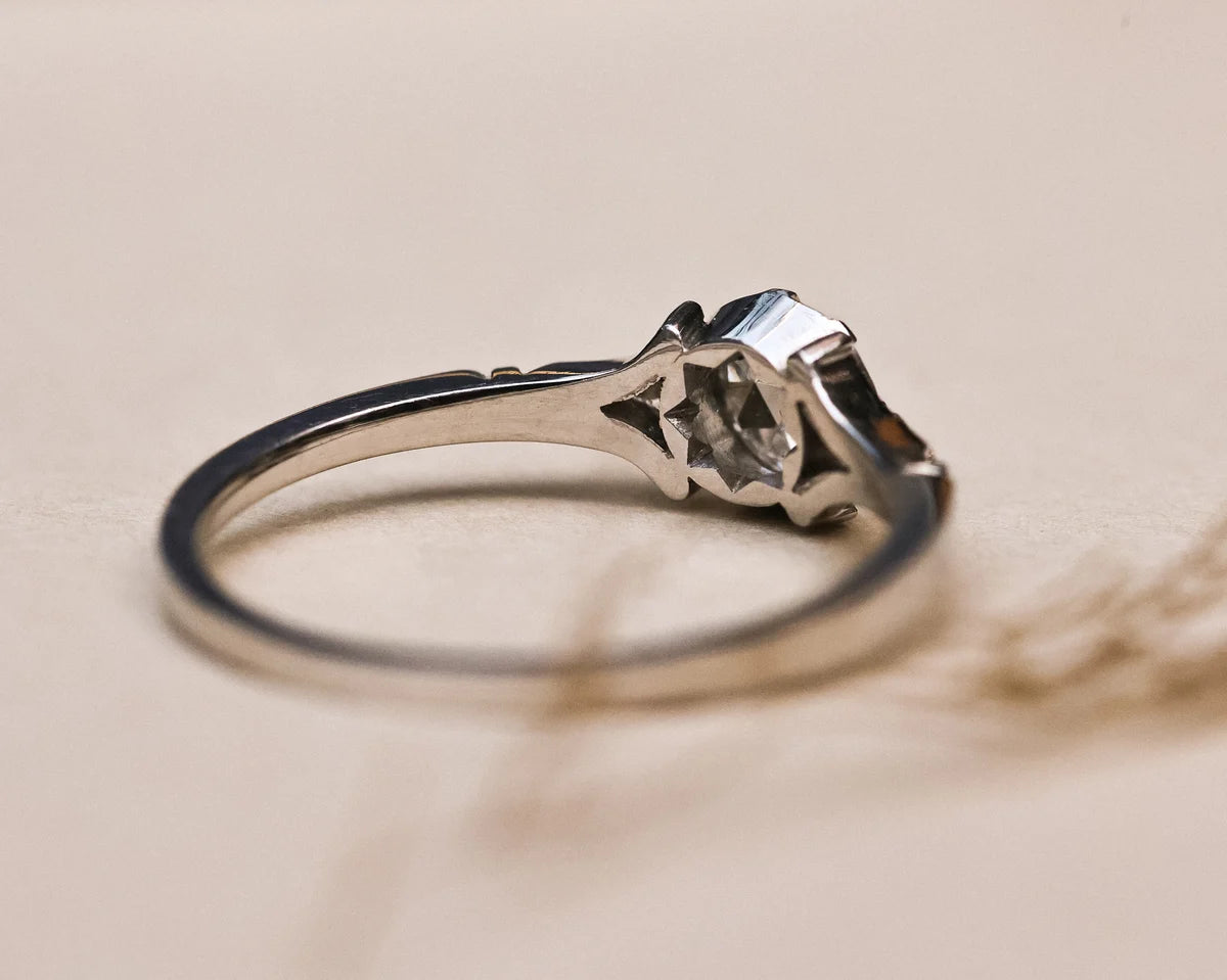 A silver-toned ring with a geometric, star-like openwork setting and a clear rectangular gemstone, photographed on a warm beige background.