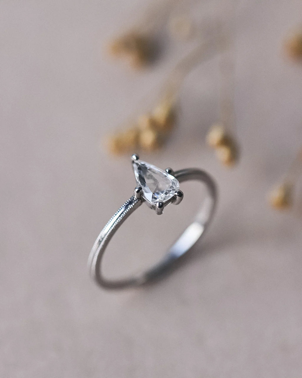 Angled close-up of pear cut diamond ring with milled edge band