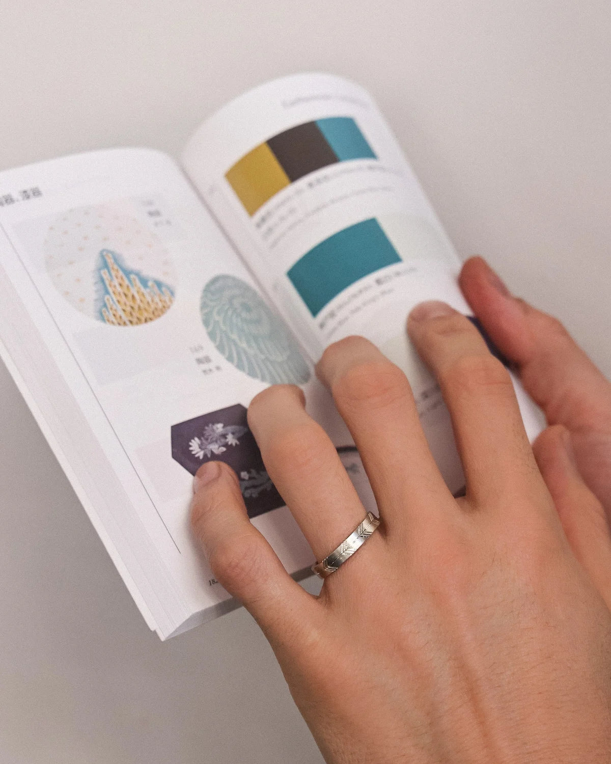 Hand holding a cylindrical product with color swatches next to an open book on a neutral background