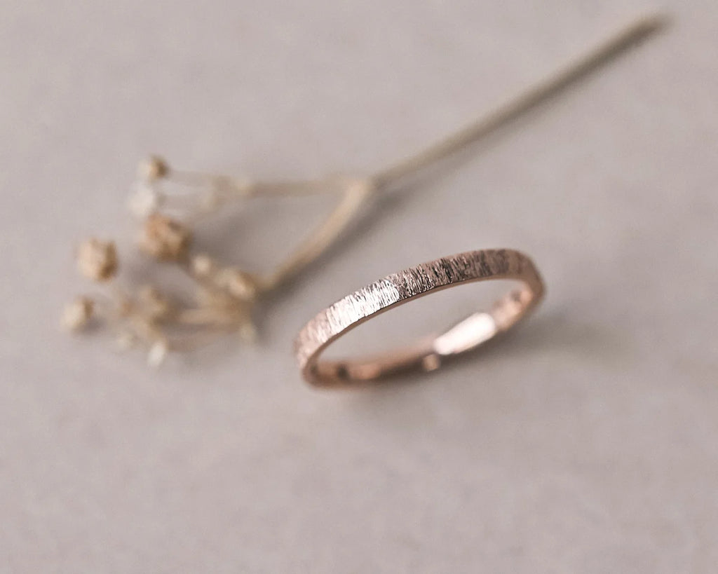 Angled view of 18ct rose gold horn texture wedding ring with dried flowers