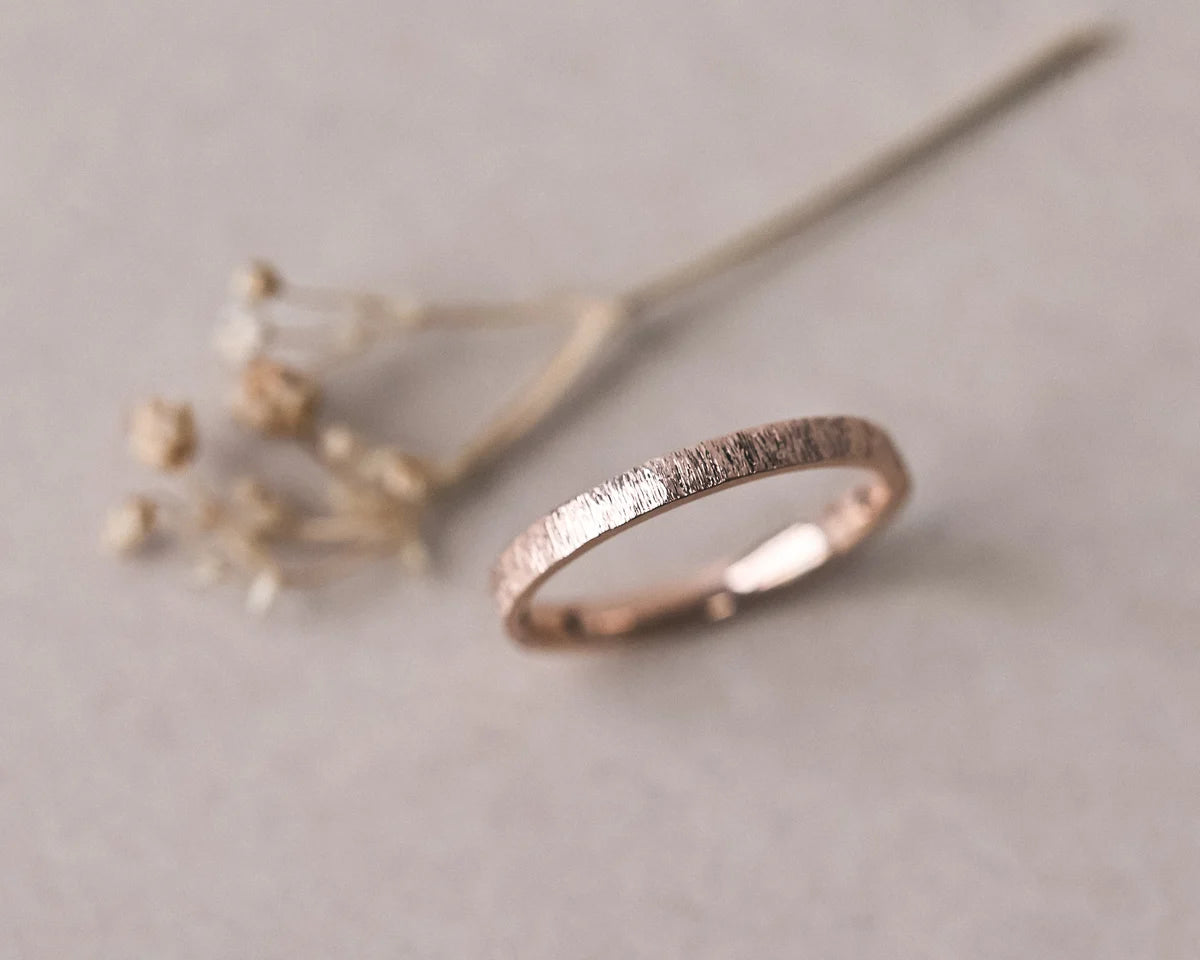 Angled view of 18ct rose gold horn texture wedding ring with dried flowers